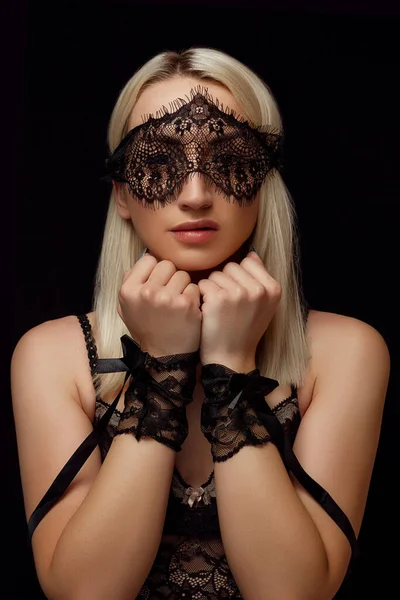 Retrato de uma jovem mulher loira bonita em uma máscara facial de renda e algemas de renda em um fundo isolado preto — Fotografia de Stock