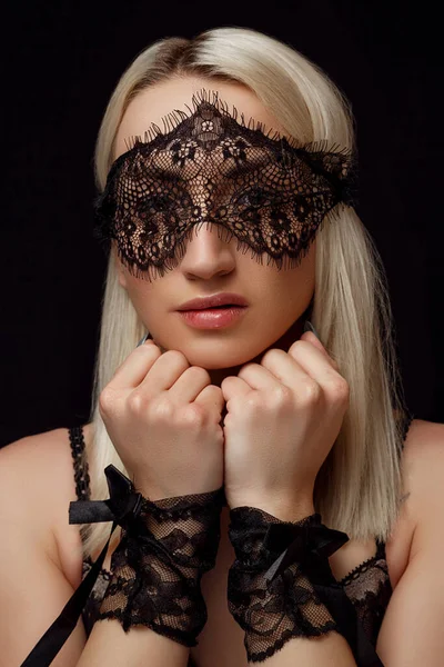 Retrato de una joven hermosa mujer rubia en una máscara de encaje y esposas de encaje sobre un fondo negro aislado — Foto de Stock
