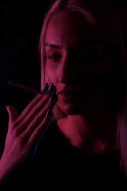 Genç, beyaz, güzel, sarışın kadın sigara içiyor. Neon ışıkta yakın plan portre