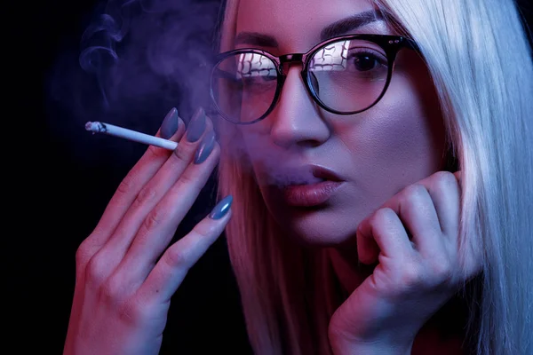 Fiatal kaukázusi gyönyörű szőke nő szemüveggel dohányzik. közelkép portré neon fényben — Stock Fotó