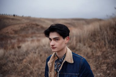 Dağların arka planında, bulutlu bir havada esmer bir gencin dramatik portresi. seçici odak, küçük odak alanı