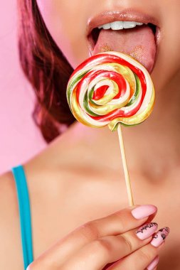 Genç ve güzel bir kız, renkli parlak bir lolipopun fotoğrafını diliyle yalıyor. pembe izole bir arkaplanda