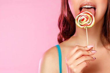 Genç ve güzel bir kız, renkli parlak bir lolipopun fotoğrafını diliyle yalıyor. pembe izole bir arkaplanda