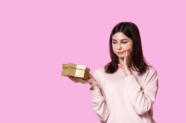 Elinde hediye kutusu olan açık renk kazaklı genç bir kız. Tatminsiz ve hayal kırıklığına uğramış. pembe izole bir arkaplanda.