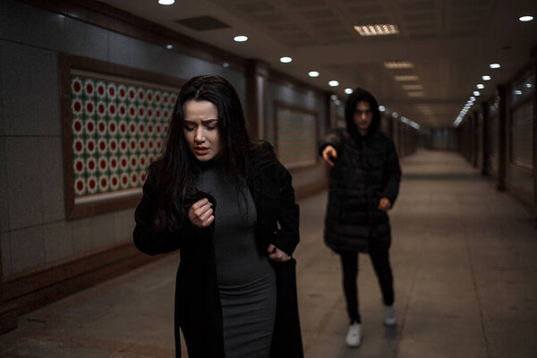 a young beautiful woman tries to escape from a robber in black clothes . in the underpass. at night