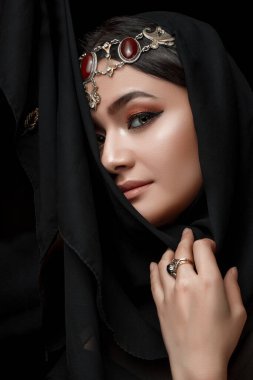 Siyahi bir stüdyo arka planında Doğu tarzı mücevherlerle süslenmiş bir kadının kavramsal ortadoğu portresi..