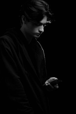  Siyah arka planda siyah kapüşonlu, elinde cep telefonu olan genç bir adam.