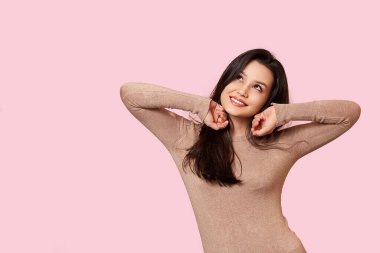 Açık kahverengi kazaklı güzel bir esmer gülümsüyor. pembe izole bir arkaplanda