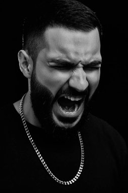 Genç, ciddi bir adamın dramatik portresi. Müzisyen, şarkıcı, siyah elbiseli, siyah izole bir arka planda sakallı rapçi. Öfkeyle, öfkeyle bağırıyor..