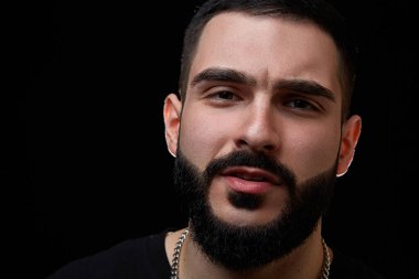 Genç, ciddi bir adamın dramatik bir portresini yakın plan çekiyoruz. Müzisyen, şarkıcı, siyah elbiseli, siyah izole bir arka planda sakallı bir rapçi..