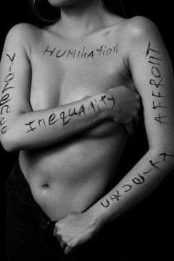Siyah zemin üzerinde hakaret, zulüm, eşitsizlik yazan genç bir kadının vücudunun bir parçası. Fotoğraf. Yazı, fotoğrafçının elinde yazan bir dövme değil..