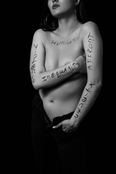 part of a young woman's body with the words affront,cruelty,inequality on a black background.photo.the inscription is not a tattoo, written by the photographer's hand.