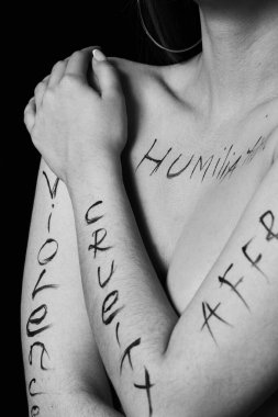 Siyah zemin üzerinde hakaret, zulüm, eşitsizlik yazan genç bir kadının vücudunun bir parçası. Fotoğraf. Yazı, fotoğrafçının elinde yazan bir dövme değil..