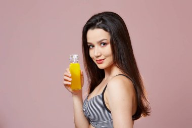 Mayo giymiş güzel, ince Asyalı bir kız. Elinde taze meyve suyuyla. Gülümsüyor. pembe izole bir arkaplanda.