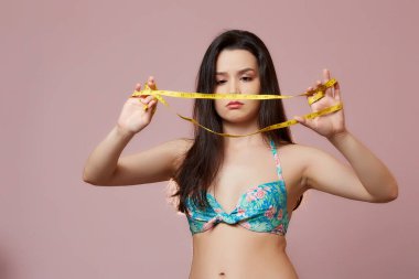 Mayo giymiş güzel, ince Asyalı bir kız. Elinde bir mezura ile. pembe izole bir arkaplanda.