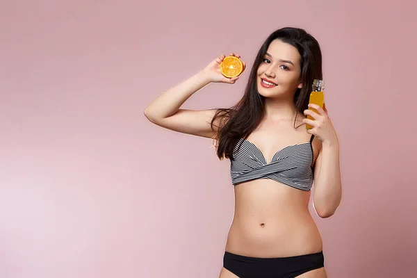 水着姿のアジア系の若い美少女 新鮮なジュースとオレンジを手に 笑顔だ ピンク色の孤立した背景で — ストック写真