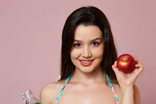 水着姿のアジア系の若い美少女 新鮮なジュースとアップルを手に 笑顔だ ピンク色の孤立した背景で — ストック写真