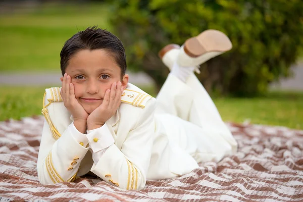 Jeune garçon de première communion couché sur une couverture sur l'herbe Images De Stock Libres De Droits