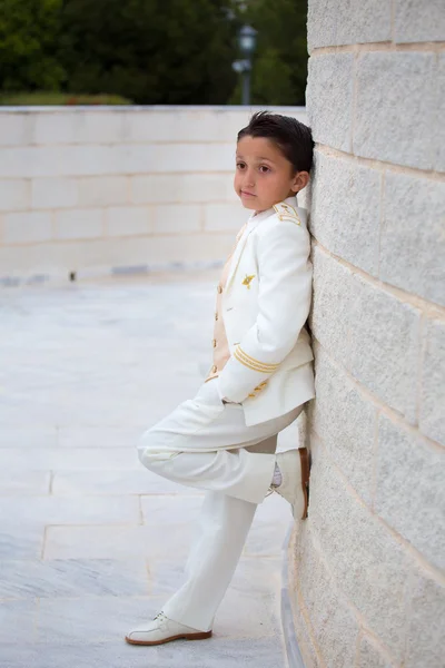 Young First Communion boy leaning on a wall with  one foot Stock Photo