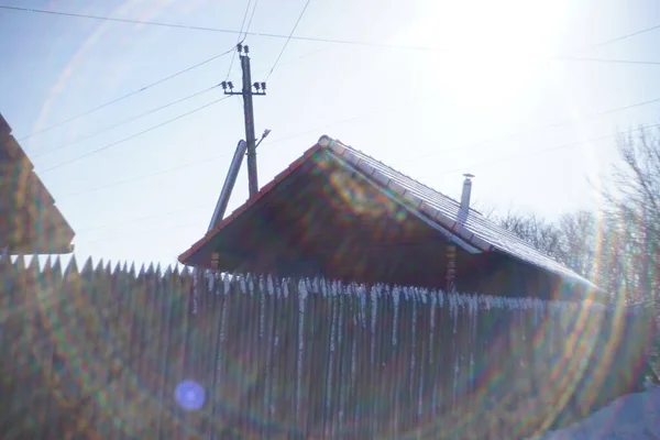 Деревянный дом с забором и электрическим столбом. Зимний солнечный день. Красивые солнечные лучи вокруг . — стоковое фото