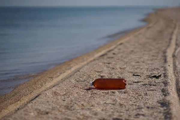Порожня пластикова пляшка лежить на морському пляжі. Екологічне забруднення. Колії на піску . — стокове фото