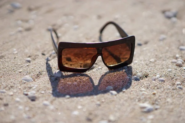 Brown sunglasses with beautifull reflection on a sandy beach. — Stock Photo, Image