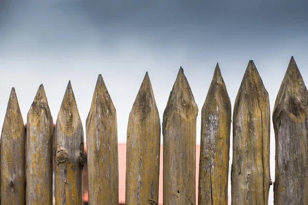 Gri gökyüzüne karşı keskin tahta kazıklardan yapılmış bir çit. — Stok fotoğraf