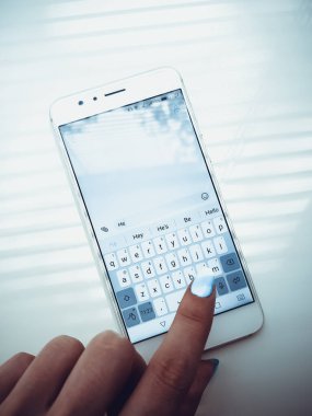 Mavi tırnaklı kadın eli beyaz bir telefona mesaj yazıyor