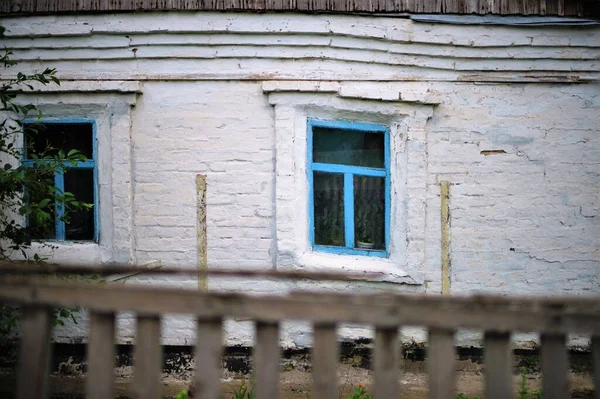Fațada unei vechi case rurale cu rame de ferestre albastre. Vechea deformare a structurii peretelui cauzată de tăcere . — Fotografie, imagine de stoc