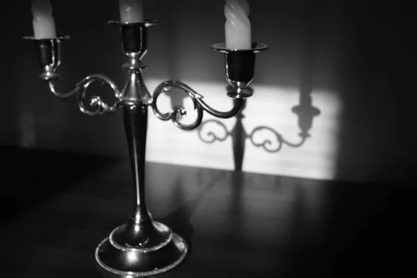 Vintage candlestick on three candles with shadow reflection on the wall. Black and white photo. — Stock Photo, Image