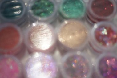 Yuvarlak plastik kutularda farklı payetler ve parıltılarla odaklanmamış arkaplan, tırnak tasarımı için malzemeler.