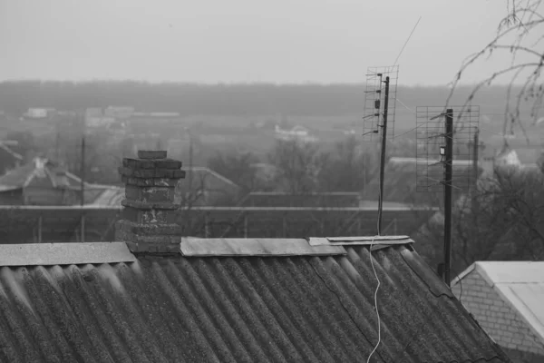 Oud landelijk dak van golfplaten van asbestcement, stenen schoorsteen en tv-antennes, bewolkte dag, landelijk landschap. — Stockfoto