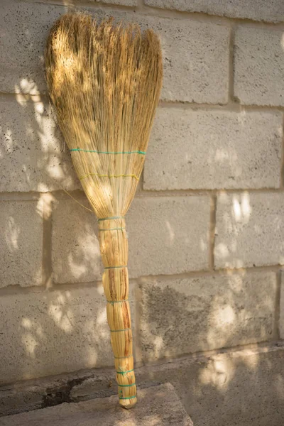 A new wicker broom stands upside down against the stone wall. — Stock Photo, Image