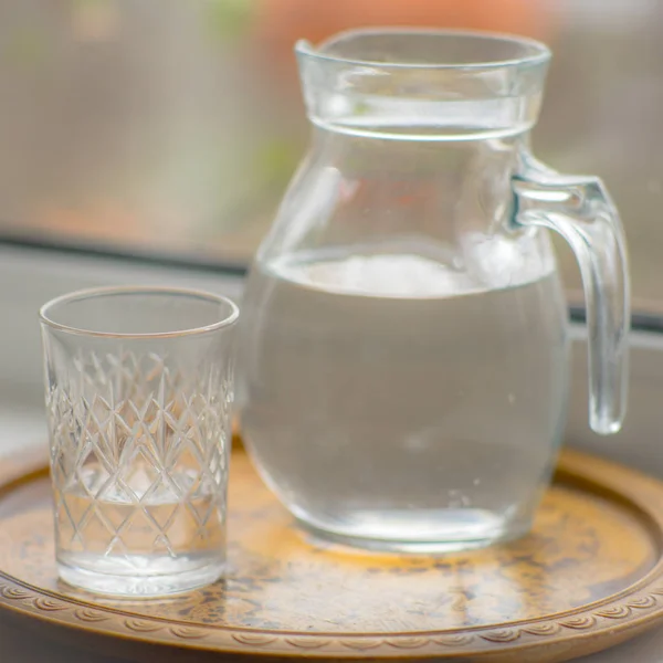 Caraffa d'acqua e un bicchiere sul davanzale della finestra . — Foto Stock