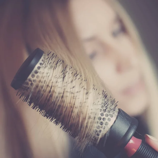 Round brushing combs long blond hair, on the background the face of a girl in blur. — Stock Photo, Image