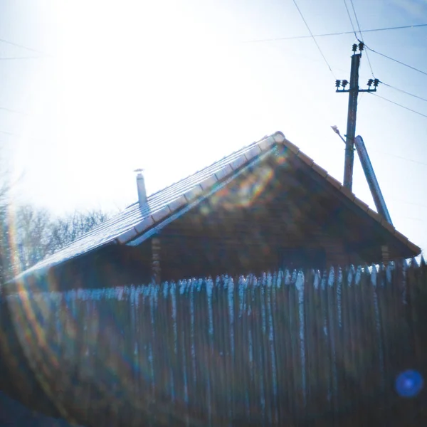 Dřevěný dům s laťkovým plotem a starým elektrickým sloupem. Zimní slunečný den. Krásné sluneční paprsky kolem. — Stock fotografie