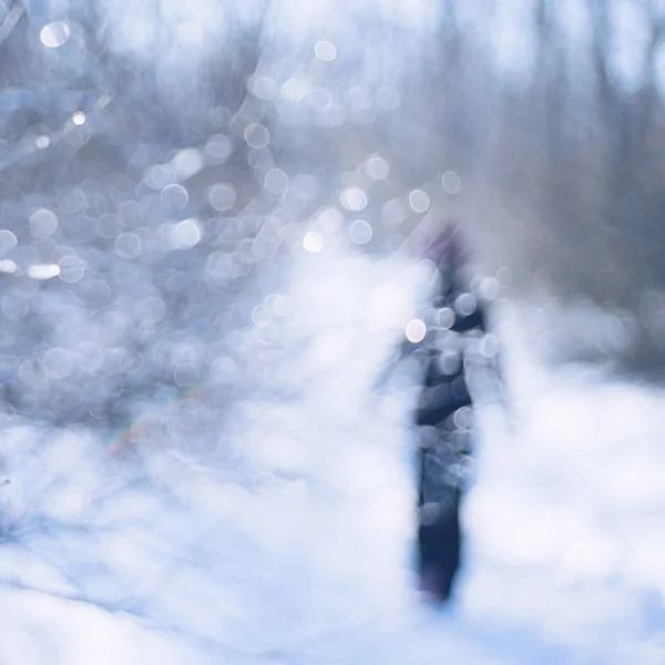 Loop door het winterbos. Silhouet van een eenzaam persoon in het zwart lopend op de weg. — Stockfoto