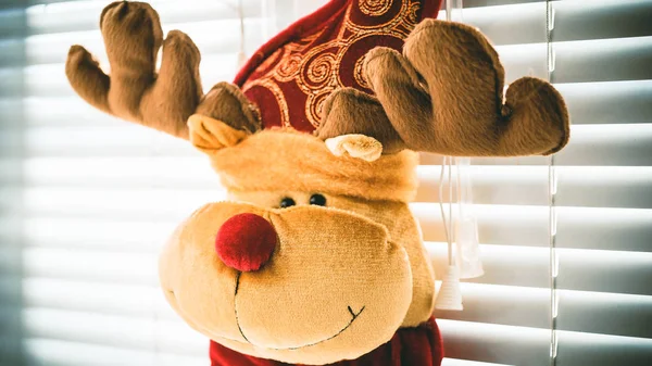 Олень с рогами, мягкая игрушка, висит на окне с жалюзи, Новый год . — стоковое фото
