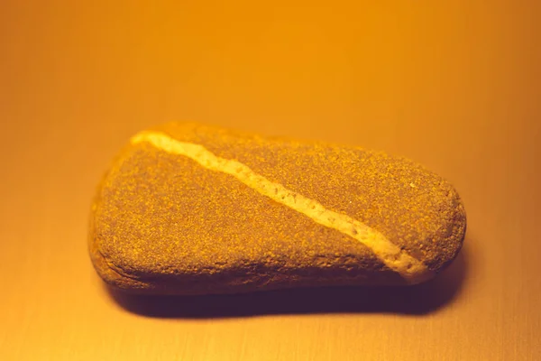 Pedra de seixo com linha branca diagonal natural na mesa, luz laranja . — Fotografia de Stock