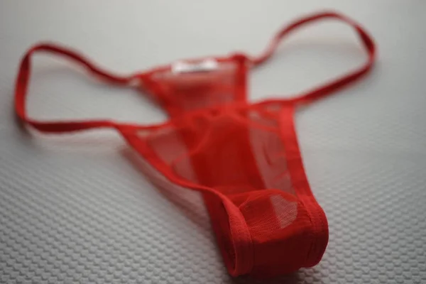 Red thong of transparent fine mesh on white fabric with embossed pattern. — Stock Photo, Image