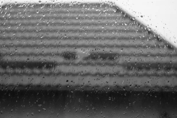 Okno v kapkách deště, kapky vody na sklo, kachlová střecha venku — Stock fotografie