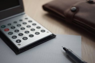 Metal katlama hesap makinesi, kağıt kalem, masada deri çanta..