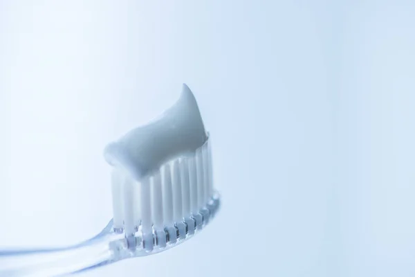 Escova de dentes de plástico transparente com pasta de dentes branca em um fundo branco azul com reflexão sobre o vidro . — Fotografia de Stock