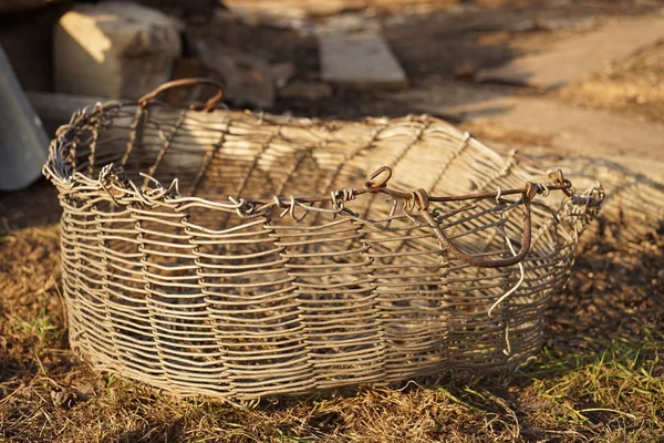 Old wicker aluminum wire basket on the ground in a rural yard.