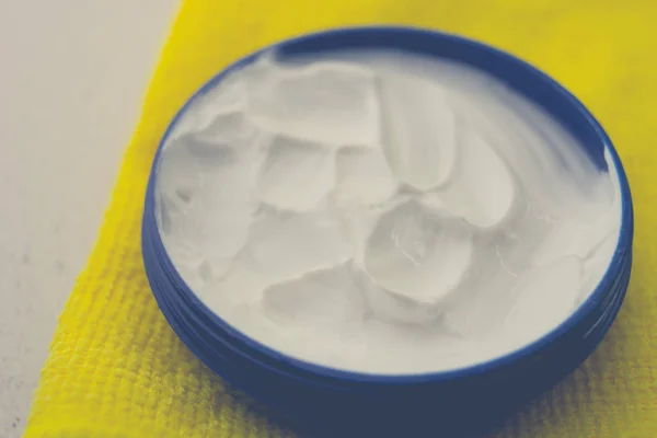 Open round container with white cream on a yellow table. — 스톡 사진