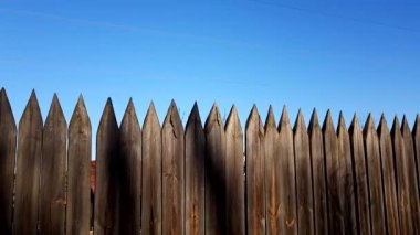 Fence made of sharp wooden stakes and blue clear sky