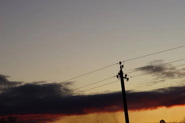 Torre elétrica de alta tensão silhueta no céu escuro do por do sol . — Fotografia de Stock