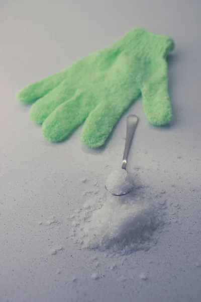 White sea salt in a spoon and green bath glove on the table. — 图库照片