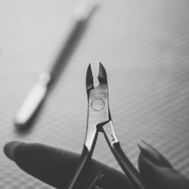 Nippers cuticle scissor in female fingers, cuticle shovel on the blurred background, bw photo.