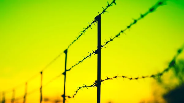 Black silhouette of a barbed wire fence in yellow sky. — Stock Photo, Image